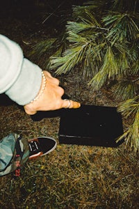 a person is pointing at a black laptop on the ground